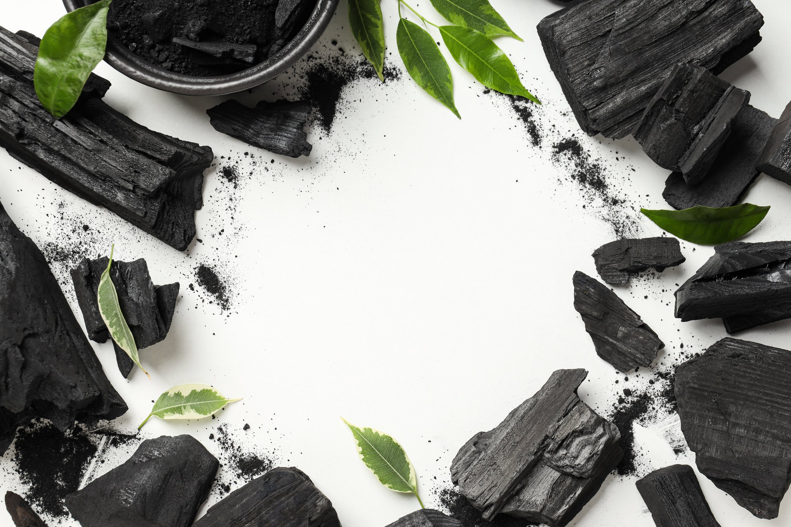 Charcoal, powdered charcoal and leaves on white background